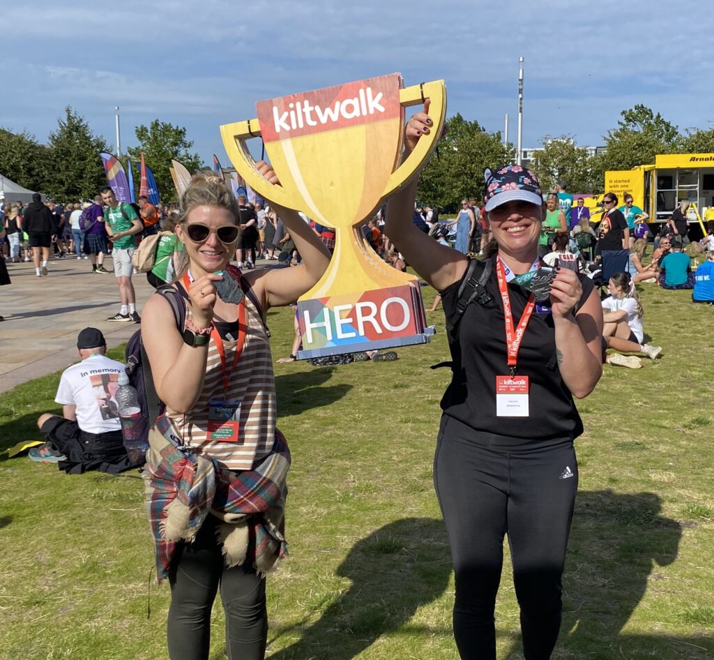 Two people holding medals and a cardboard trophy
